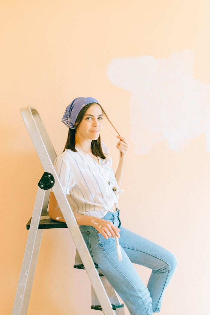 Young woman on ladder painting a wall in a bright room.